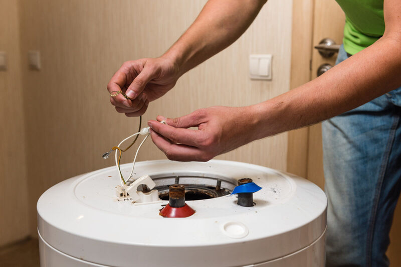 Technician working on electrical connections at the top of a tank water heater