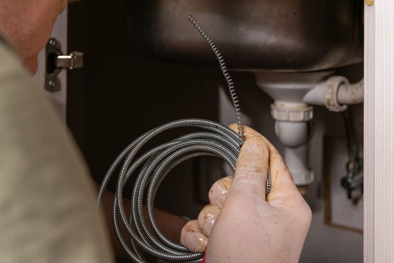 Plumber holding a coiled drain-cleaning snake beneath a kitchen sink